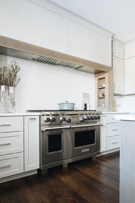 An extra-long light gray wooden range hood is fixed over oak built-in spice racks and above a stainless steel dual range mounted against white oblong cooktop tiles and flanked by light gray cabinets. Ann Sacks Backsplash, Wooden Range Hood, Light Grey Kitchen Cabinets, Kitchen Cooktop, Light Gray Cabinets, Modern Farmhouse Kitchen, Ann Sacks, White Shaker Cabinets, White Kitchen Island