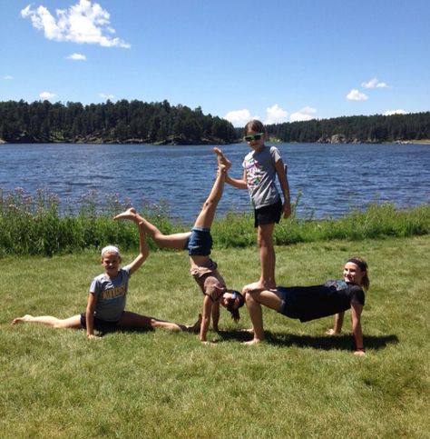 Four person acro stunt by a lake 6 Person Stunts, 4 Person Acro Poses, Yoga Challenge 4 People, Group Yoga Poses 4 People, Four Person Stunts, 4 Person Yoga Poses, Yoga Poses For 4 People, 4 People Stunts, 4 Person Stunts