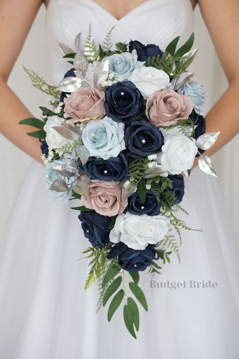 This lovely assortment of navy blue, dusty blue and mauve roses is bound to turn heads on your wedding day. This lovely cascading brides’ bouquet from the is an absolutely breathtaking arrangement for any bride to be, in any season. Bright greenery and silver accent jewels and foliage complete the look and add a delicate realism to this beautiful bouquet. This bouquet is 10” wide, 18” long, and is crafted by our in-house florists without using a foam base to anchor the flowers to the bouquet. In Bride Bouquets Blue, Wedding Flowers Navy Blue, Small Bridesmaid Bouquets, Fake Wedding Flowers, Mauve Roses, Sage Eucalyptus, Fresh Wedding Flowers, Cascading Wedding Bouquets, Blue Bride