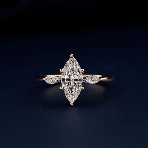 This exquisite 14K gold marquise cut lab-grown diamond engagement ring features a 1.00CT center stone in a breathtaking F/G color and VVS2/VS1 clarity.  Two shimmering 0.20CT marquise side stones complete the timeless trilogy design. Handmade by our skilled artisans, this ring is a symbol of love and ethical brilliance.  IGI certification is available upon request. Marquise Cut Diamond Engagement Rings, Meaningful Gifts For Her, Anniversary Rings For Her, Marquise Diamond Engagement Ring, Ring Inspo, Trilogy Ring, Stone Wedding, Lab Grown Diamonds Engagement, Dream Engagement Rings