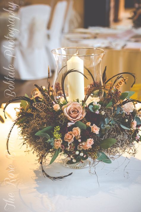 Nude rustic woodland hurricane lantern table centre piece with moss and pheasant feathers.  Captured by Bobtale Photography Winter Wedding Centre Pieces, Pheasant Flower Arrangements, Pheasant Feather Decor Wedding, Wedding Flowers With Pheasant Feathers, Pheasant Feather Wedding Bouquet, Pheasant Feather Wedding, Floral Arrangement With Pheasant Feathers, Winter Wedding Table, Winter Wedding Centerpieces