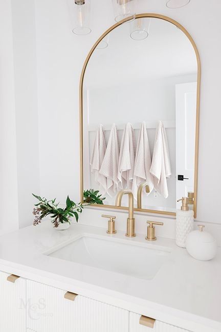 Vancouver bathroom renovation by Love Sims Home  Gold arched mirror, gold hardware and faucet, soft pink towels on hooks Small Bathroom Gold Hardware, Arch Gold Mirror Bathroom, Burlington Gold Bathroom, Large Gold Mirror Bathroom, Gold Arched Bathroom Mirror, Gold Mirror In Bathroom, Bathroom Remodel Gold Hardware, Gold Accent Powder Room, Gold Mirror For Bathroom