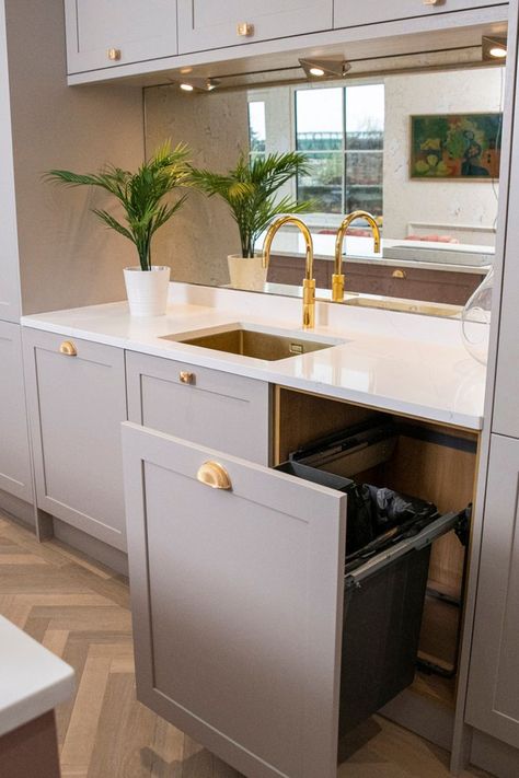 Kitchen with slim-shaker doors in a neutral cashmere tone, ornate brass gold cup handles, white worktop, brass gold quooker tap, gold sink, antique mirror splashback, pull out bin storage solution, plant, oak herringbone flooring Cashmere Kitchen White Worktop, Timber Shaker Kitchen, Cashmere Kitchen Shaker, Cashmere And Green Kitchen, Pink Shaker Kitchen, Wren Cashmere Shaker Kitchen, Dusky Pink Kitchen, Cashmere Kitchen Colour Scheme, Cashmere Shaker Kitchen