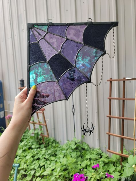 Bring an eclectic spooky vibe to your home with our purple spiderweb. This piece features a rhinestone spider (this can be omitted by request) delicately dangling from her web. Each web has a variety of purple stained glass, each boasting their own unique patterns, textures, iridescence, and opacity.  The web casts a beautiful refraction of purple light as the sun moves behind it throughout the day. Hang your web in a window corner or doorway corner, or use it as an accent piece of wall art. We love customizing with different color requests; please message us to discuss your custom color request prior to purchasing.  Overall size, specific glass used, and placement of glass may vary slightly, as each web is hand made to order. Please note photos are of previously completed designs. We stri Spider Web Stained Glass Window, Stained Glass Art Halloween, Stained Glass Spiderweb, Spooky Stained Glass Art, Stained Glass Witchy, Goth Stained Glass Art, Spooky Suncatchers, Unique Stained Glass Ideas, Halloween Stained Glass Patterns