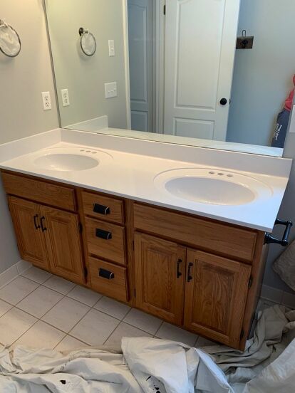 My builder grade Master Bathroom vanity was bad. Really bad. After two years I finally decided to do something about it and got to work. Here’s a before photo of the bathroom. Break Out the Spray Cans I used a can of Rustoleum Matte Black spray paint I had in the basement on the light fixture for a quick, easy and free light refresh! Cover Everything! For the countertop I purchased a $4.00 can of Rustoleum Appliance Epoxy spray paint from Walmart. I heard it produced lots of overs… Spray Paint Light Fixture Black, Rustoleum Appliance Epoxy Spray On Countertops, Epoxy Spray Paint Countertop, Master Bath Black Vanity, Builder Grade Vanity Makeover, Rustoleum Appliance Epoxy, Bathrooms With Black Vanities, Bathroom Black Cabinets, Black Bathroom Cabinet