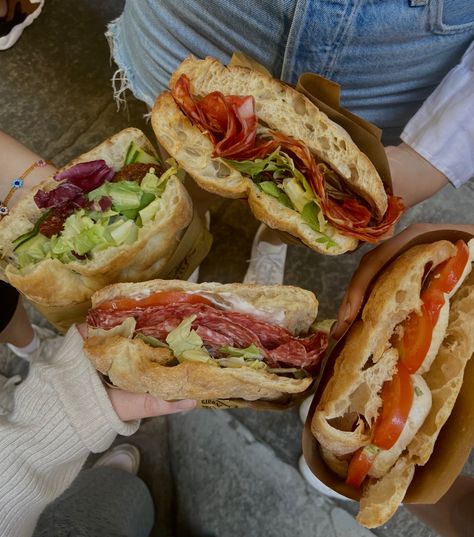 Four hands holding four different Panini with different toppings. They contain salami, tomatoes, salad, cream cheese and mozzarella. Foods In Italy, Italy Aesthetic Travel, Italian Food In Italy, Italy Food Aethstetic, Panini Aesthetic, Italian Summer Food, Italian Food Truck, Italian Fast Food, Food Moodboard