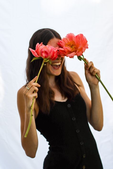 Girl holds two pink peony flowers over her eyes and is smiling hugely. Her the photo is cropped below her waist. She is wearing a skinny black dress with front buttons and has brown hair. Sheet Photoshoot, Indoor Photoshoot, Creative Shoot, Smelling Flowers, Pinterest Photography, Test Shoot, Instagram Flowers, White Sheet, Branding Shoot