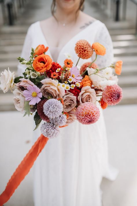 Bride in white lace dress holds a colorful bouquet towards the camera. Bouquet is full of bright blooms in orange, purple and mauve colors and tied with an orange ribbon. Pansies Wedding, Petunia Wedding Bouquet, Bouquet Of Pansies, Pansy Bridal Bouquet, Pansy Arrangements, Wedding Reception Flowers, Unique Wedding Photos, Pansies Flowers, Wedding Ceremony Flowers