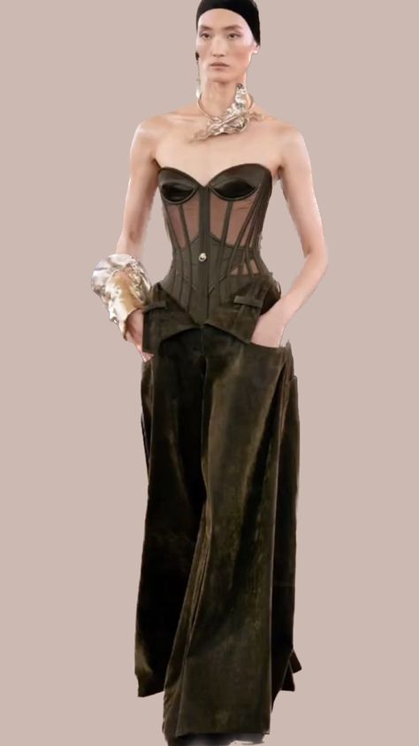 Bi-material corset in bronze satin and tulle laced up at back with gold brass eyelets and extra- wide trapeze pants in thick bronze velvet twill enhanced by a belly-revealing “unbuttoned” low-cut. Gold-plated metal cuff inlaid with molded half-face and ear elements embellished with rhinestone piercings. Choker necklace in silver-plated metal inlaid with molded elements of leaf and ear embellished with rhinestone piercings and cultured pearl. Half Face, Fall 2023, Gold Brass, Tulle Lace, Low Cut, Piercings, Choker, Silver Plated, Choker Necklace