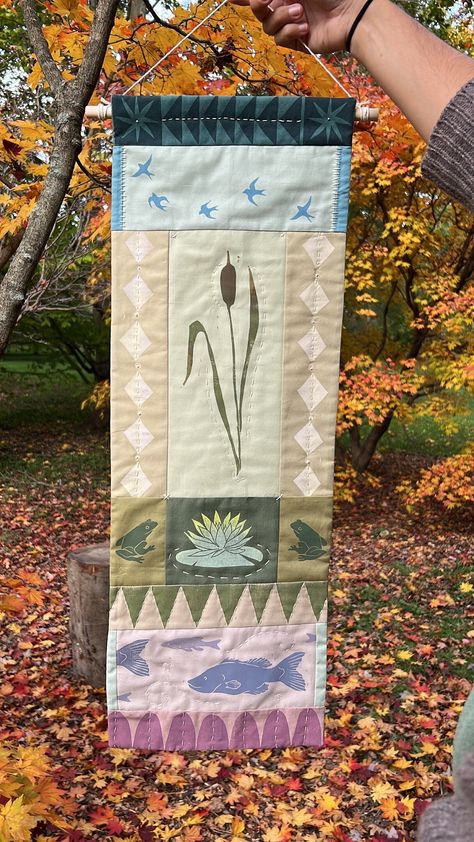 "Step into a serene pond landscape, where nature's symphony comes alive in this handcrafted wall hanging. Inspired by traditional quilting motifs, this piece showcases block-printed panels and a medley of patchwork fabrics, capturing the essence of pond life. A graceful cattail sways, playful frogs leap, fish shimmer in the water, and birds soar through the air. Each element is lovingly hand-quilted, adding depth and dimension. Rich textures, contrasting patterns, and vibrant colors evoke the se Quilt On Wall Decor, Vertical Wall Hanging, Quilt Block Wall Hanging, Sewn Wall Hanging, Quilt On Wall, Quilted Banner, Plant Quilt, Quilt Tapestry, Nature Quilt