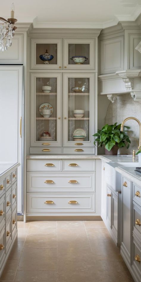 A close-up view of light gray kitchen cabinets with glass-front doors, displaying beautifully styled dishware. The cabinets feature intricate molding details and bronze hardware. Gray Owl Cabinets Kitchens, Cabinets With Glass Doors Kitchen, To The Ceiling Kitchen Cabinets, Bm Edgecomb Gray Cabinets, Kitchen Cabinets With Glass Doors On Top, Tall Kitchen Cabinets Ideas, Full Wall Kitchen Cabinets, Gray Kitchen Cabinet Ideas, Glass Upper Kitchen Cabinets