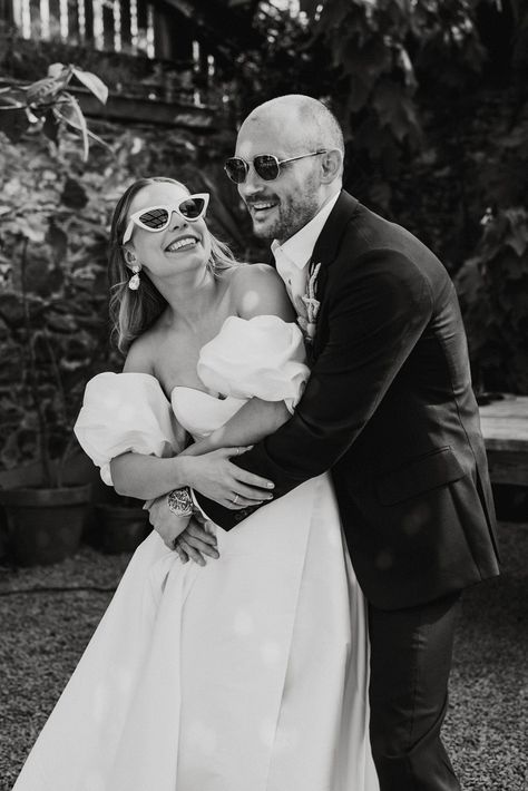 Groom wearing sunglasses hugs the bride from behind in a puff sleeve wedding dress with white sunglasses Bride White Sunglasses, Wedding Pictures With Glasses, Sunglasses With Wedding Dress, Bride And Groom Sunglasses Photo Ideas, Bride With Sunglasses Photo Ideas, Wedding Dress Sunglasses, Bridal Party With Sunglasses, Bride In Sunglasses, Engagement Shoot Sunglasses