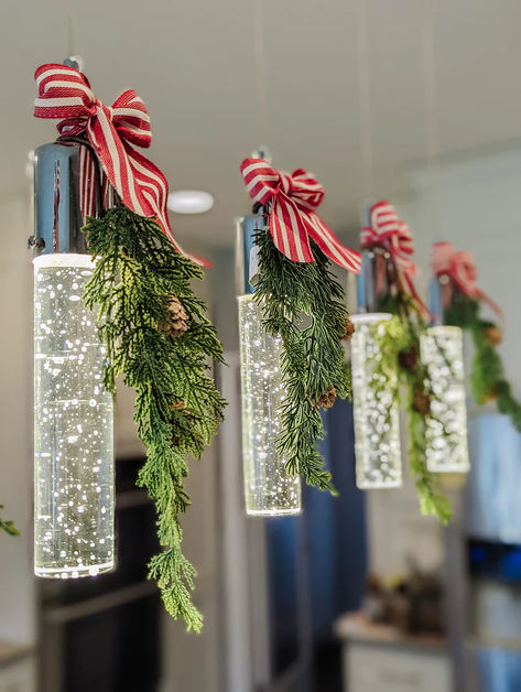 I helped a friend decorate for the holidays and her kitchen is a showstopper! We achieved this charming look by adorning her pendant lights with picks of greenery and added a little bow to hide the stem and bring it all together. Pendant Christmas Decor, Christmas Decor On Pendant Lights, Christmas Lights Above Kitchen Cabinets, Christmas Decor Pendant Lights, Decorate Pendant Lights For Christmas, Decorating Pendant Lights For Christmas, Pendant Light Christmas Decor, Christmas Pendant Light Decor, Lights Over Kitchen Island