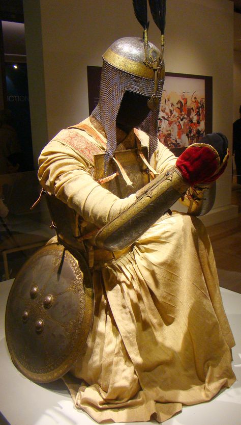 Indian armor, khula-khud (helmet), char aina (curaiss), dastana (vambrace/arm guard), dhal (shield), a traditional Sikh warrior outfit from the nearly 80 historical artefacts on display in central London at the world's first major exhibition on the Golden Temple of Amritsar, north India. A full-sized mannequin of a Sikh warrior dressed in the way a high-ranking warrior would have been at the height of the Sikh Empire, head to foot in original, ornate, gold body armour and weaponry. Indian Armor, Sikh Warrior, Warrior Dress, Body Armour, Warrior Outfit, Ancient Armor, Historical Armor, Arm Guard, Golden Temple