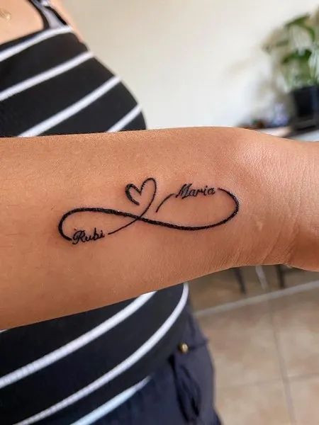 Infinity Tattoo With Names Infinity With Names Tattoo Designs, Wrist Tattoos For Women With Names, Tattoo Names Idea, H Name Tattoo Designs, Tattoo Name With Design, Mommy Of Two Tattoos, Infinity Tattoo With Kids Names On Wrist, Heart And Name Tattoo Ideas, Infinity Tattoo With Year