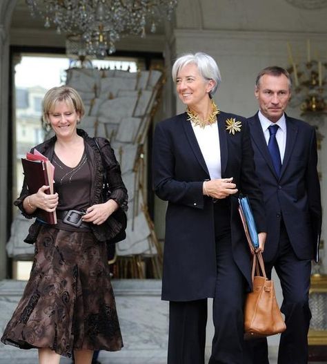 But the prize for the most virtuosic deployment of the work uniform today goes to Christine Lagarde, the French lawyer who runs the International Monetary Fund. Her tailored dark (black or charcoal) suits are accessorized with a great haircut, dangling pearl earrings, and an Hermès scarf. That’s it. She’s nearly 60 and succeeds in looking both female and powerful without seeming to overthink either. Never has so little looked like so much. Christine Lagarde Style, Lagarde Christine, Charcoal Suits, Christine Lagarde, Draped Coat, Business Professional Outfits, Work Uniform, White Collared Shirt, Printed Scarf