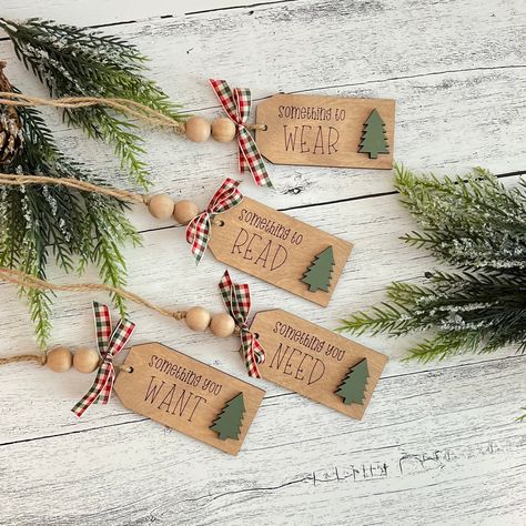 Give a gift with purpose this year with our wooden gift tags! Each set includes four tags:  1. Something To Read 2. Something To Wear 3. Something You Want 4. Something You Need Tag Dimensions: Height: 1.75 inches Length: 3.5 inches Depth: .25 inches Each tag is finished off with bead accents and a red, green and white bow!  Please Note: You are purchasing the set of four tags only. The accessories are used for staging purposes only. Christmas Wood Tags Diy, Wood Gift Tags Diy, Wooden Gift Tags Christmas, Wooden Tags Ideas Diy, Gift Tags Diy Handmade, Cricut Gift Tags, Christmas Gift Tag Ideas, Wooden Christmas Tags, Gift Tag Ornaments