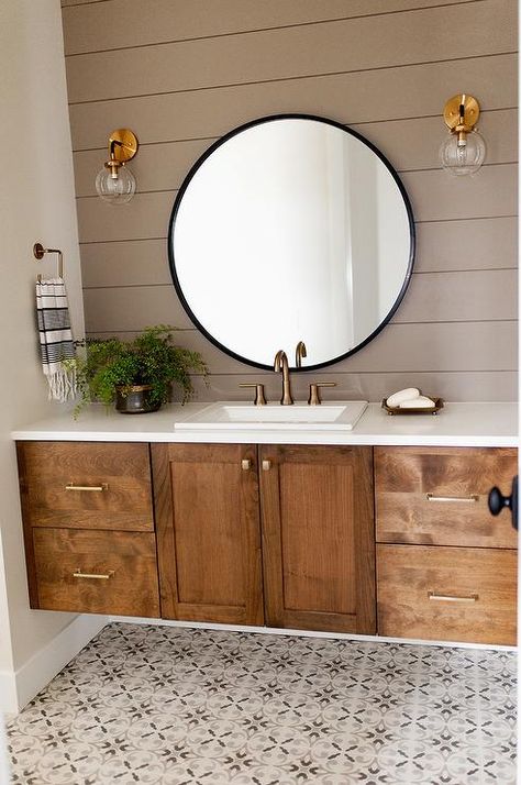 This charming bathroom boasts a brow shiplap wall lit by two brass and clear glass globe sconces mounted on either side of a round black mirror hung over a brown oak washstand. Unique Bathroom Vanity, Renovation Design, Bathroom Pictures, Bathroom Design Luxury, Stylish Bathroom, Wooden Cabinets, Ship Lap Walls, Bath Remodel, Farmhouse Bathroom