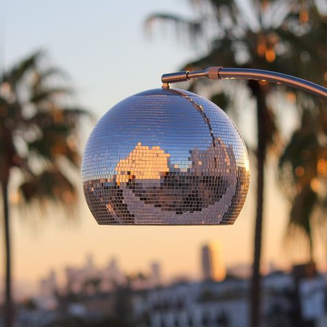 Elevate your space with this sparkling disco ball floor lamp, where hundreds of tiny mirrors are meticulously individually hand-placed on the lamp shade here in Los Angeles! The lamp is TWO-IN-ONE - enjoy a sparkling light show in direct sunlight or soft lighting in the evening. Each tiny mirror is sealed in place with white grout. The heavy faux marble base weighs 15 pounds to ensure the lamp can withstand any adjustments. The height adjusts from 61 to 70 inches, and the shade position from 25 to 38 inches. Included is a 5 foot cable with a convenient foot switch and standard E26 socket. The lamp comes bundled with an LED light bulb for your immediate enjoyment. Please note that this product is made with real glass pieces and may have sharp edges, so watch your hands when adjusting the la Disco Ball Office, Ball Floor Lamp, Tiny Mirror, Disco Floor, Disco Decor, Tiny Mirrors, Disco Ball Mirror, Cosmic Design, White Grout