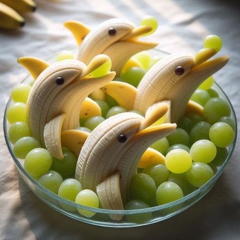 A creative display of bananas and grapes arranged to resemble dolphins swimming in a clear dish. Each banana is cut at the stem end to mimic a dolphin's mouth, holding a green grape as if it's a ball. The bananas are slightly curved, enhancing the dolphin-like shape, and small dark spots are used to create eyes. Around the banana dolphins, a layer of green grapes is scattered, simulating water, filling the dish. The lighting is natural and soft, Dolphin Bananas And Grapes, Banana Dolphins, Dolphins Swimming, Green Grape, Meaningful Art, Creative Display, Green Grapes, Bananas, Dark Spots