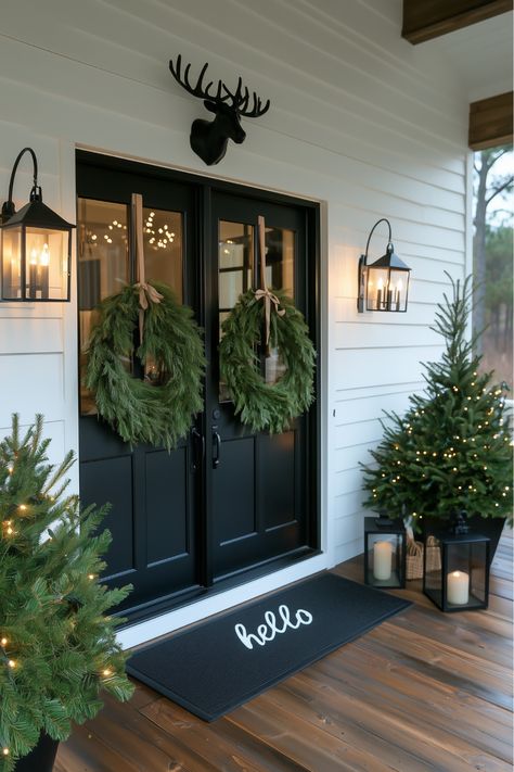 If you adore simplicity, this minimalist farmhouse porch is perfect. A simple wreath and soft candle lanterns bring a cozy touch to a neutral color palette. Wouldn’t it be peaceful to sit on a clean, modern porch surrounded by holiday lights? It’s understated yet festive—Christmas porch decor in its purest form. Modern Farmhouse Christmas Decor Porch, Simple Christmas Exterior Decor, Modern Farmhouse Outdoor Christmas Decor, Christmas Decor Ideas Outdoor Farmhouse, Minimalist Christmas Porch Decor, White Farmhouse Christmas Decor Exterior, Minimal Christmas Outdoor Decor, Minimalist Christmas Front Porch, White And Black Porch