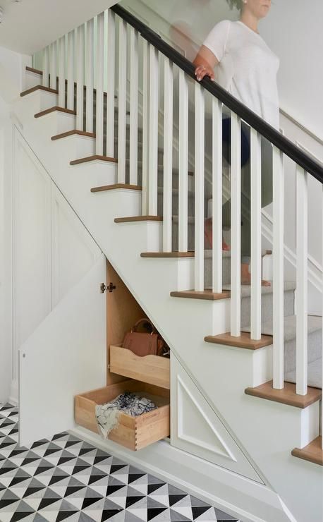 A contemporary foyer staircase features built-in storage fitted with easy access pull-out drawers hidden behind decorative wainscoting alongside a black and gray diamond print tiled floor. Closet Under Stairs, تحت الدرج, Vstupná Hala, Foyer Staircase, Open Trap, Stairs Storage, Diy Staircase, Staircase Storage, Under Stairs Cupboard