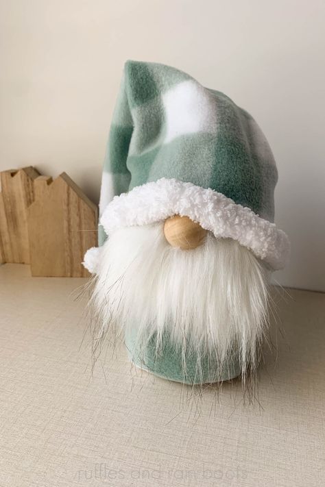 Green and white fleece gnome with a white trim and white beard on a linen background with small wooden houses. Gnome Shoe Patterns Free, Gnome Clothes Free Pattern, Sock Gnomes Diy How To Make No Sew, Sock Gnomes Diy, No Sew Gnome, Door Stopper Diy, Diy Bean Bag, Sock Gnomes, Fabric Door Stop