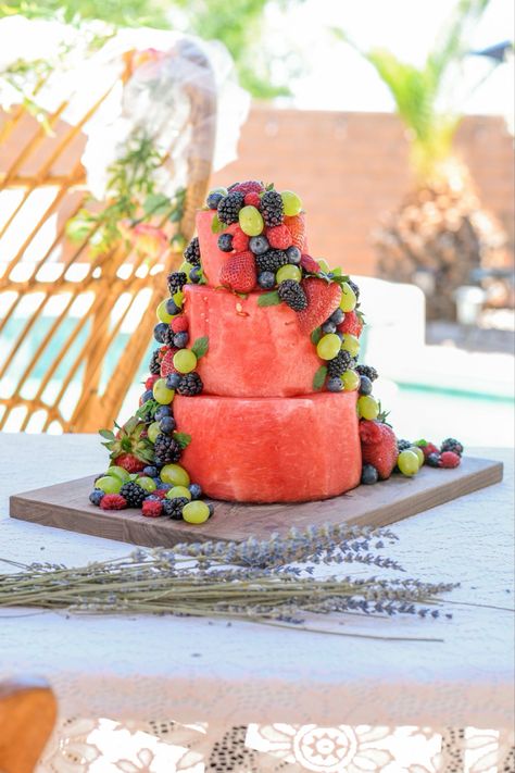 A three tiered cake made out of watermelon and adorned with grapes, blueberries, raspberries,  strawberries, and mint.