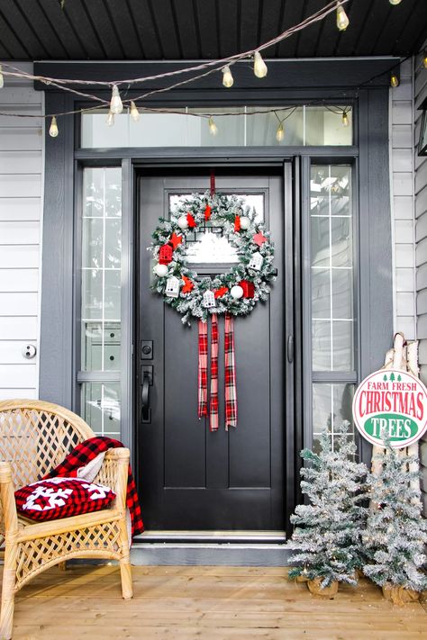 a flocked Christmas evergreen wreath with red and white ornaments and red plaid, hangs on a black door. next to the door are mini flocked trees and a chair with plaid blankets Red And White Ornaments, No Spend, Plaid Blankets, Flocked Trees, Home And Decor, Evergreen Wreath, Pretty Life, Fresh Christmas Trees, Christmas Porch Decor