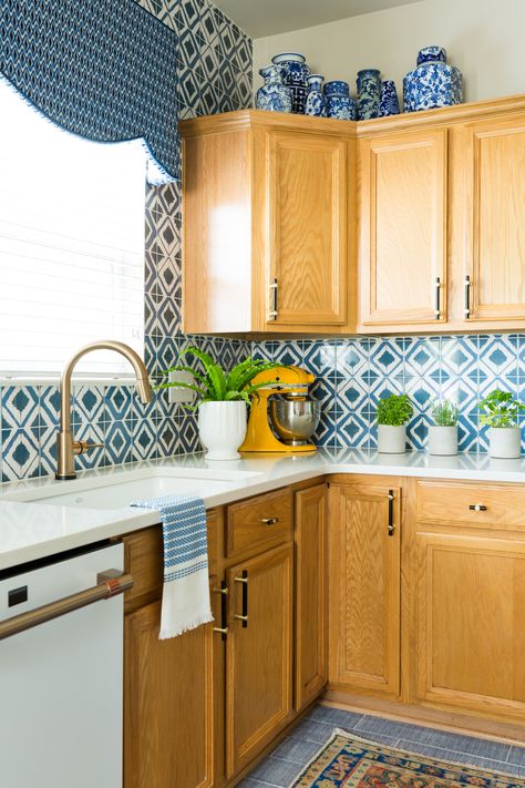 Probably the biggest surprise to many in this project was my decision to NOT paint my honey oak cabinets. Do I regret it? NOT A CHANCE! I love the warmth and depth they add to the space. The modern black hardware from Schaub made such a difference! They are complemented so well with my blue geometric backsplash for The Tile Shop and the custom blue cornice above my sink. The white countertops tie it all together. #bluebacksplash #bluewindowcornice #dwellbycheryl #honeyoakcabinet #honeyoak Oak Cabinets With Blue Backsplash, Honey Oak Countertop, Wood Cabinets With Blue Backsplash, Kitchen Tile With Oak Cabinets, Honey Maple Kitchen Cabinets Modern, Blue Backsplash Kitchen Wood Cabinets, Honey Oak Cabinet Black Hardware, Blue Kitchen With Oak Cabinets, Blue Tile Backsplash Kitchen Oak Cabinets