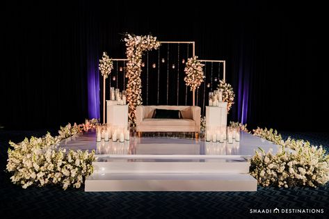 Bride and groom seating for this Indian destination wedding reception- a neutral loveseat atop a white platform with three various-sized gold modern rectangles covered in white florals and greenery with hanging candles Sangeet Sitting For Bride And Groom, Couple Seating For Sangeet, Bride And Groom Seating, Couple Seating, Hard Rock Riviera Maya, Weddings In Mexico, Indian Destination Wedding, Destination Wedding Reception, Purple Room