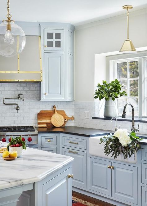 Farmhouse sink under a kitchen window surrounding honed black granite countertops and light blue cabinets with antique brass knobs lit by Katie globe pendants. Kitchen With Blue Cabinets, Countertops Ideas, Light Blue Kitchens, Серая Кухня, Black Granite Countertops, Black Countertops, Blue Kitchen Cabinets, Blue Cabinets, White Marble Countertops