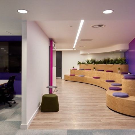 Tiered Seating Zone | Office Design and Collaboration | Morgan Lovell | These cool, curved auditorium-style benches are great for breakout meetings or for large Town Hall meetings or presentations. Colourful pink and purple cushions provide cool office branding whilst wood surfaces and planters bring a more natural feel to the space to enhance wellbeing. #Collaboration #BreakoutArea #TieredBenches #OfficeDesign #OfficeInteriorDesign Curved Office Design, Tiered Seating Office, Best Office Design, Kids Church Rooms, Lounge Room Design, Auditorium Design, Meeting Room Design, Tiered Seating, Auditorium Seating