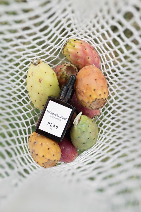 Bird's-eye view of a meticulously arranged net bag containing ripe prickly pear fruit and a bottle of precious prickly pear seed oil, showcasing the beauty and natural allure of PEAU's skincare ingredients Prickly Pear Fruit, Prickly Pear Seed Oil, Prickly Pear Oil, Luxurious Skincare, Pear Fruit, Beauty Elixir, Pear Cactus, Prickly Pear Cactus, Net Bag