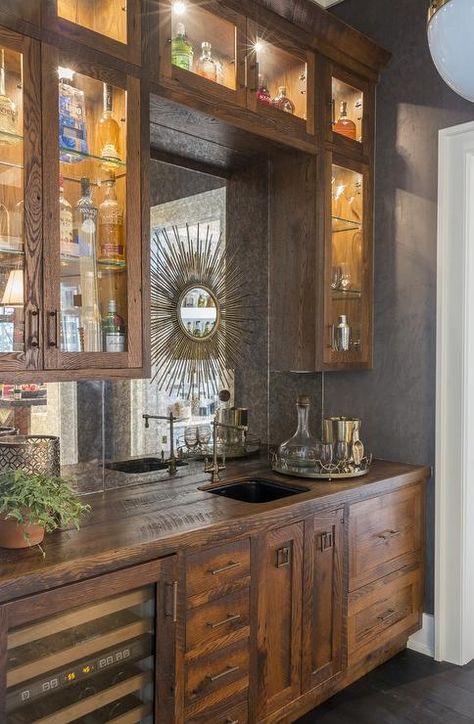 Rustic wet bar features rustic cabinets fitted with a glass-front wine cooler paired with distressed wood countertops fitted with a bar sink and vintage style swing-arm faucet. Antique Mirror Backsplash, Palmetto Bluff Homes, Mirrored Backsplash, Rustic Sink, Farmhouse Backsplash, Beadboard Backsplash, Mirror Backsplash, Dark Wood Cabinets, Herringbone Backsplash