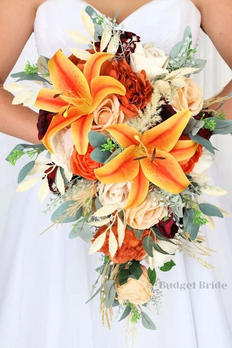 This is a cascading brides bouquet with burnt orange, apricot and champagne roses accented with orange lilies, mixed greenery and pampas grass. All of our wedding bouquets are made with artificial wedding flowers. Fall Wedding Bouquets Lilies, Tiger Lily Bouquet Wedding Fall, Tiger Lily And Rose Bouquet, Flowers For Orange Prom Dress, Tiger Lily Wedding Cake, Champagne And Orange Wedding, Tiger Lily Wedding Decor, Orange Lily Wedding Bouquet, Orange Flowers For Wedding