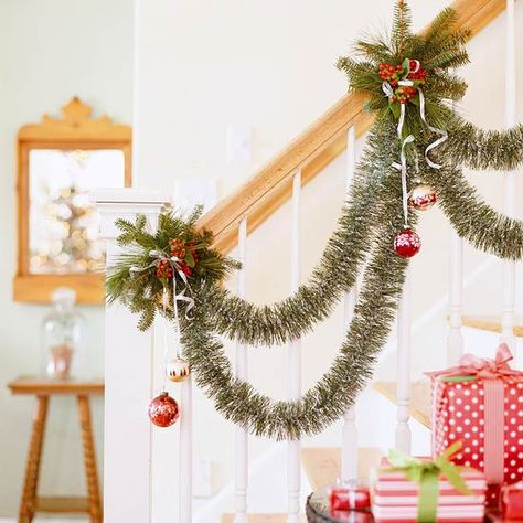 Stairway Showcase Garland  Stairway Showcase Garland  For a twist on the traditional garland-dressed banister, try this accent. Wire double swags of green tinsel garland at intervals along the banister rail, and tie ornaments dangling from silver ribbon. To add clusters of greenery and holly, tightly wrap wire around the railing for each cluster and tuck cuttings securely beneath the wire. Stairway Garland, Christmas Banister, Christmas Stairs Decorations, Christmas Stairs, Green Tinsel, Winter Wonderland Decorations, Christmas Staircase, Diy Christmas Garland, Christmas Decorations Cheap