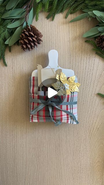 Life Stylishly - Home Decor on Instagram: "LIKE ♥️ and SAVE this post if you want to see more easy but Elevated gifting ideas   Comment SHOP for links to everything you need to recreate this stunning hostess gift! 🎁✨  Here’s how I made it: I started with a mini marble cheeseboard and folded a plaid tea towel to create a pocket. * Fold the tea towel in half, then fold it in half again to create a long rectangle. * Wrap the towel around the cheeseboard, securing it snugly around the back.  * Next, I tied it all together with a green velvet ribbon for an elegant touch. * In the front pocket, I tucked in cheese knives and finished the look with a gorgeous gold poinsettia ornament for that extra holiday sparkle. 🌟  Perfect for holiday parties or as a thoughtful hostess gift that will impress! Cheeseboard Gift Wrapping, Tea Towel Gift Wrap, How To Wrap A Charcuterie Board As A Gift, Tea Towel Folding Gift Ideas, Hand Towel Gift Ideas, Cheese Board Gift Ideas, Craft Trailer, Towel Gift Ideas, Thrifted Gifts