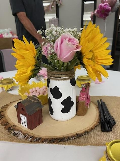 Cowgirl baby shower. Cow print mason jar with the rim rapped in twine filled with sunflowers, pink roses and baby's breath. I received so many compliments on this simple decor. Cow Mason Jar Centerpieces, Pink Western Centerpiece Ideas, Cow Print Centerpiece Ideas, Cow Print Mason Jar Centerpiece, Cow Birthday Party Centerpieces, Pink Cow Print Baby Shower Ideas Girl, Cow Print Decorations Birthday Parties, Cow And Sunflower Baby Shower Theme, Country Girl Baby Shower Ideas