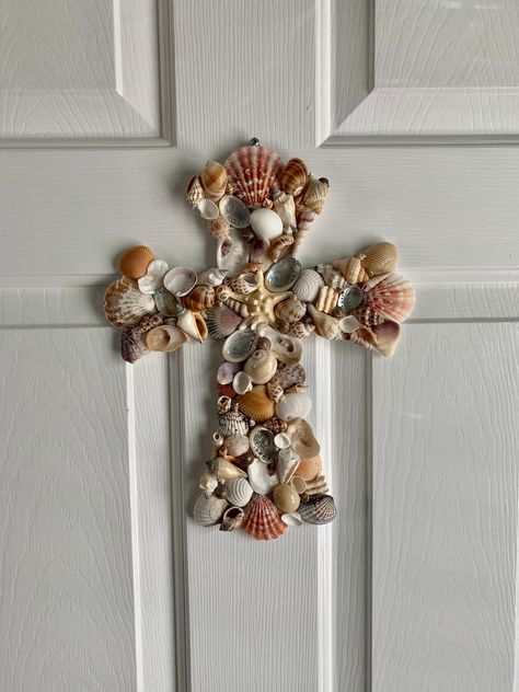 "This beautiful, handcrafted coastal seashell cross is guaranteed to add a tranquil touch to your coastal home wall decor. The cross is adorned with a variety of seashells found along the coast of North Carolina, featuring abalone shells and a starfish at the center.  Measures 12\" l x 9\" w Seashells securely attached with high quality weather resistant glue.  Cross is hand painted white.  Each seashell design varies while maintaining the same style and beauty. Recommended for indoor use or wel Cross With Shells, Seashell Ladies, Sea Shell Crafts Seashell Art, Seashells Crafts, Easter Wreath Cross, Wood Crosses Diy, Seashell Wall Decor, Wooden Cross Crafts, Beach Wreaths