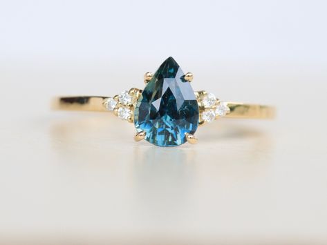 Get ready to fall in love with this stunning pear shape teal sapphire diamond ring, where artistry and craftsmanship come together to create a one-of-a-kind piece of jewelry.  The center stone is a beautiful 1.15 carat pear-shaped teal sapphire that sparkles with the beauty of the Green forest. The diamond on either side of the center stone add an extra touch of glamour and elegance. Handmade with 14k yellow gold, this ring is a true masterpiece that is built to last. The gold band is crafted with precision to create an elegant and comfortable fit that you can wear all day long. It's the perfect choice for an engagement ring, wedding band, or a special gift for someone you love. The band is specially design to fit any kind of diamond band. Order now to experience the beauty and elegance of Pear Shaped Engagement Rings Sapphire, Saphire Engament Ring Pear Shape, Green Sapphire Engagement Ring Pear, Pear Shaped Sapphire Ring, Sapphire Engagement Ring Unique, Peach Sapphire Rings, Diamond Ring Wedding, Green Sapphire Engagement, Green Sapphire Engagement Ring