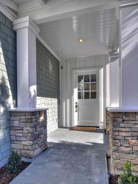 White columns wrapped at the bases with stone and soft-blue siding come together beautifully on the exterior of this coastal-inspired home. Walkway landscaping and a covered entryway with traditional white columns create inviting curb appeal. White House Wood Pillars, Adding Stone To Porch Columns, How To Build Stone Pillars Columns, Wood Columns With Stone Base, Stone Veneer Exterior, Exterior Columns, Columns (home), Front Porch Columns, Blue Siding