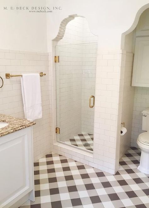 White and brown bathroom features white subway tiles that dominate most of the walls lined with a brass towel bar alongside white and brown buffalo check pattern tile floor. A walk in shower is clad in white subway tiles on walls and white and brown plaid tiles on shower floor placed next to an alcove filled with a toilet under a cabinet. Bathroom Brown Tile, Plaid Floor, Bathroom Brown, Brown Tile, White Subway Tiles, Patterned Floor Tiles, Brown Bathroom, Bathroom Floor Tiles, Rustic Bathroom