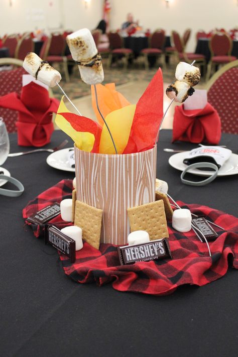 S’more and Camping Inspired Centerpieces -I used cardboard bird feeders (tops cut off) and Kleenex boxes from Michaels and wrapped with wood grain paper. Sand weighs down the box/gives placement to skewers. Dehydrate marshmallows prior. Put marshmallows onto skewer first and roast. Spray with matte finish spray paint which helps keep the ash from burning from falling off. Add some tissue paper for a fire affect and then place on top of sleeping bag like material with other S’mores-like goodies. Christmas Camping Theme, Camp Party Table Decor, Camping Theme Table Decorations, Montana Themed Party, One Happy Camper First Birthday Centerpiece, Camp Theme Centerpieces, Happy Trails Retirement Party, Camping Retirement Party Ideas, Campfire Centerpiece Ideas