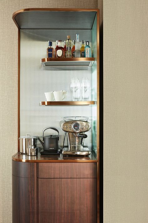 A hotel bar and espresso set up, with one shelf holding an array of liquors, the second shelf holding glasses, and the bottom holding a nice silver espresso machine, electric tea kettle, and a bucket for ice. Hotel Room Coffee Station, Hotel Room Mini Bar, Mini Bar Hotel, 2025 Design, Luxembourg Gardens, Modern Interior Decor, Hotel Website, Beauty Clinic, Glass Of Champagne