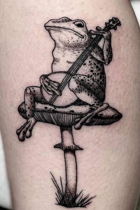 Black and grey illustrative realism thigh tattoo of a frog playing a banjo on a mushroom done by Danny Schreiber at The Copper Wolf Playing Guitar Tattoo, Banjo Tattoo, Frog Banjo, Frog Playing Guitar, Frog Playing Banjo, Mandala Hand Tattoos, Mushroom Tattoo, Planet Tattoos, Mushroom Tattoos