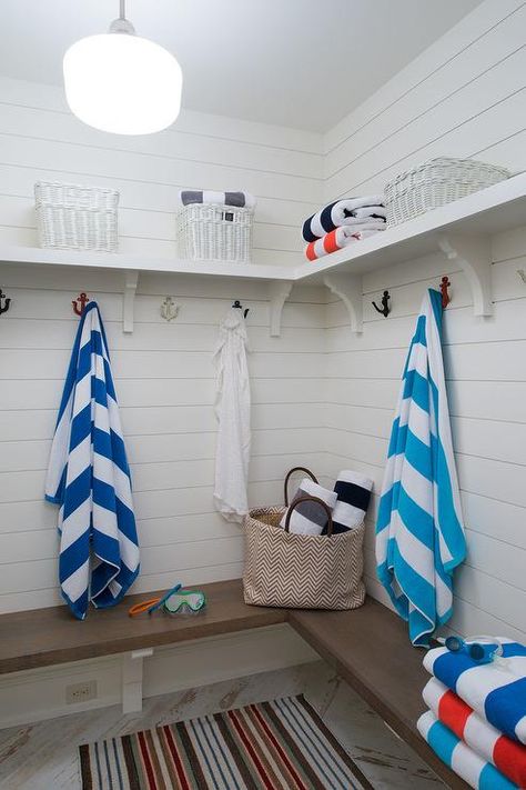 A brown striped rug sits on a plank herringbone floor in front of an l-shaped wood bench fixed against a white shiplap wall and beneath a white shelves illuminated by a white schoolhouse pendant. Outdoor Pool Bathroom Ideas, Poolhouse Bathrooms, Pool House Changing Room, Pool Bathroom Ideas, Outdoor Pool Bathroom, Pool Changing Room, Laundry/mudroom Ideas, Cottage Laundry Room, Yankee Barn Homes