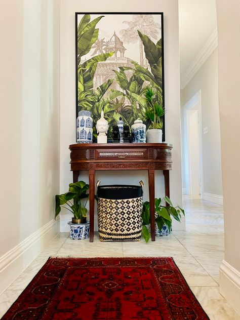 The end of a passage/hallway in British colonial style, with an antique end table, blue and white ginger jars, a tropical print and lots of greenery. The rug is Persian. British Colonial Decor Living Room Blue And White, Tropical British Colonial Interiors Bedroom, British Colonial Decor West Indies Tropical Style, British Colonial Entryway, Tropical Entryway Ideas, Tropical Colonial House, Tropical Colonial Interior, West Indies Style Bedroom, British Colonial Artwork