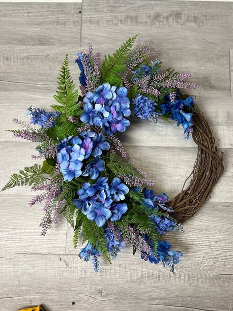 Introducing our exquisite 24x25 inch grapevine wreath, a stunning celebration of nature's beauty with its vibrant blue and purple hydrangeas paired with a delightful variety of light purple and blue florals. Each element is carefully selected to create a harmonious and enchanting composition that will captivate any observer.The addition of fern greenery adds a touch of freshness and lushness to the wreath, enhancing its natural appeal and creating a lovely contrast against the colorful blooms.Th Flower Reef, Spring Wreaths For Front Door Diy, Hydrangea Wreaths, Blue Hydrangea Wreath, Hydrangea Wreath Spring, Purple Hydrangeas, Floral Door Wreaths, Spring Floral Wreath, Purple Wreath