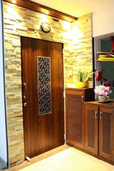 Entrance Wooden 🚪 Door with Metal Jali in Center & S.S Handle, Stone Cladding on Entrance Wall, Wooden False Ceiling on top with Spot ✨ Lights & Floor Mounted Wooden Shoe Cabinets with Louvered Doors & Décor Flower Vases on top of it - GharPedia Flat Front Door Decor, Gril Doors, Entrance Panelling, Entrance Door Design Indian, Door Elevation, Metal Jali, Wooden False Ceiling, Flat Front Door, Entrance Door Decor